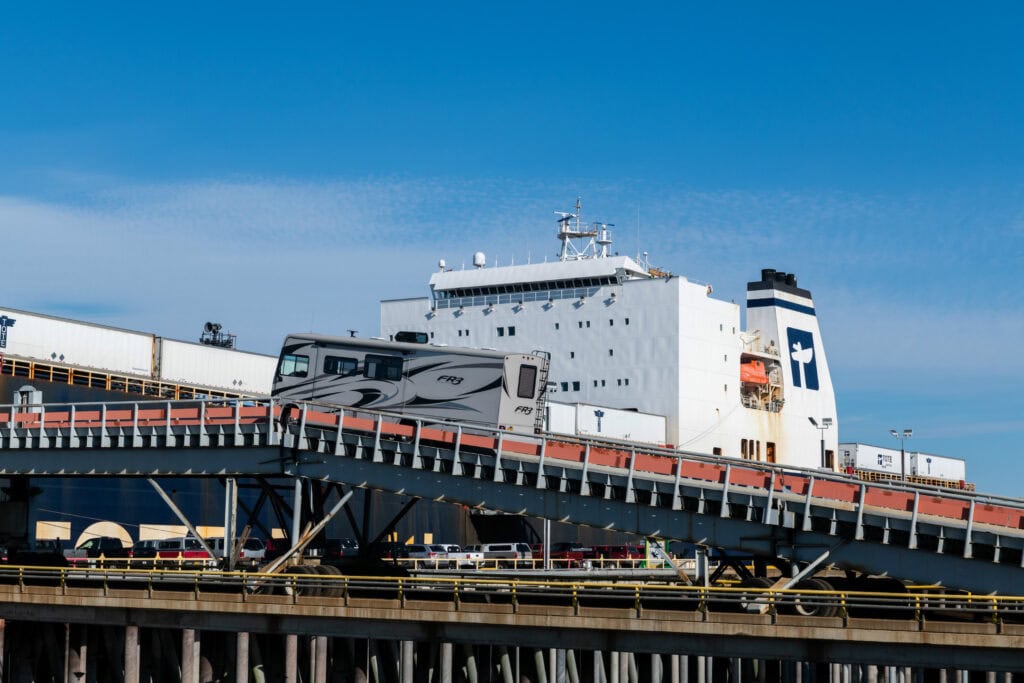 Large white cargo ship docked at port with blue sky background.