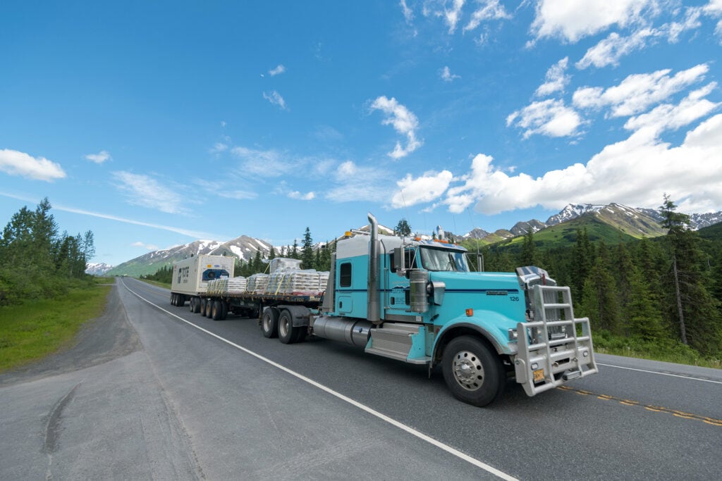 Semi-truck with a trailer carrying goods on a mountain road.