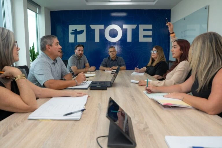 Group of people in a meeting room with TOTE logo on the wall behind them.