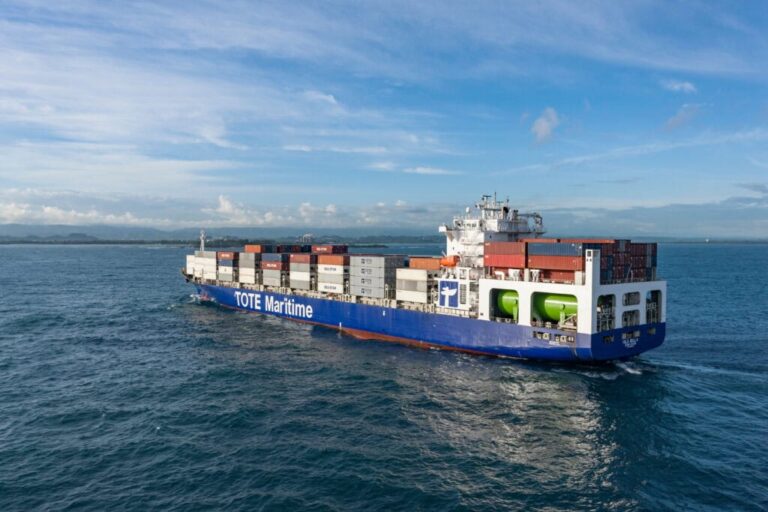 Large cargo ship with containers sailing on the ocean under a blue sky.