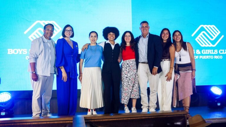 Group of eight diverse people standing on stage with a blue background.