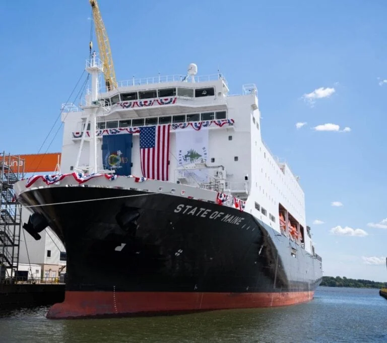 National security vessel with Maine flag docked at port under blue sky.
