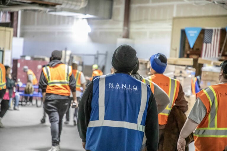 Workers in safety vests and jackets inside an industrial warehouse.