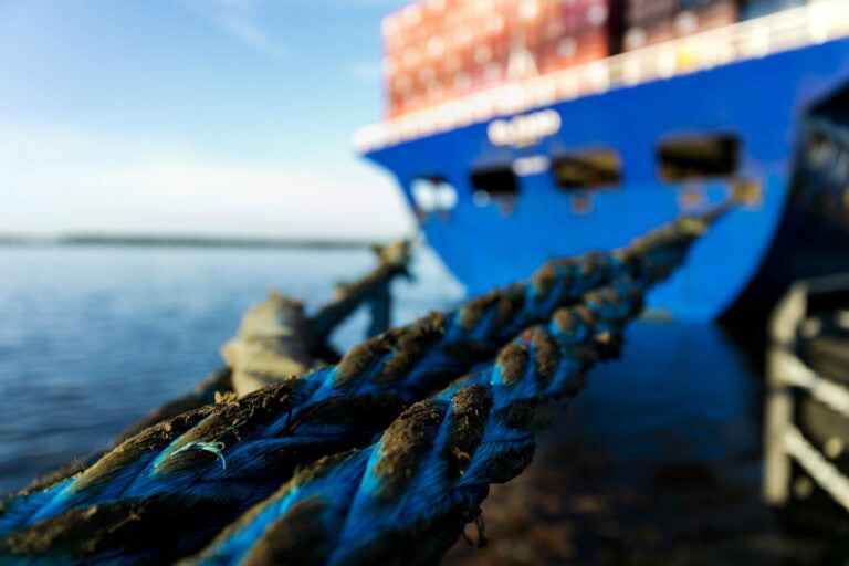 Thick, weathered rope tied to a dock in front of a large cargo ship.
