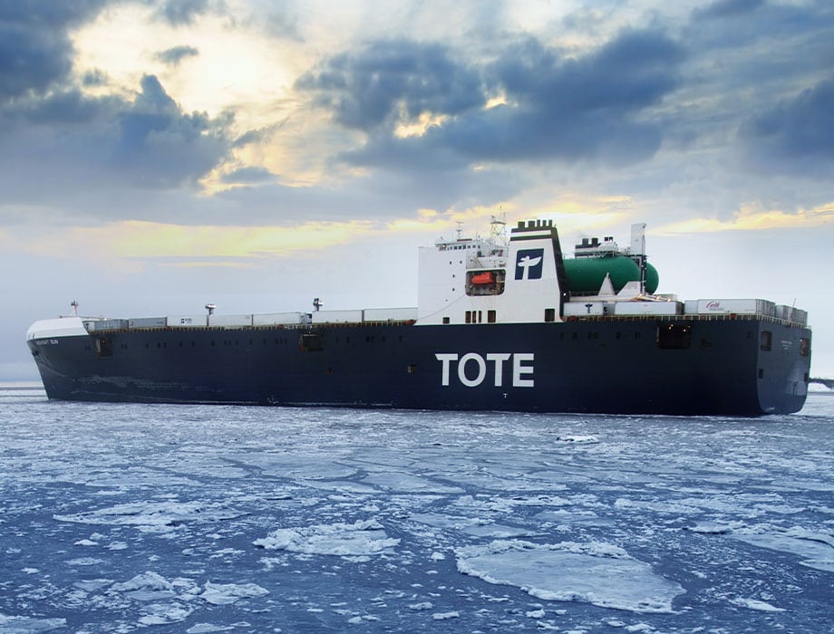TOTE cargo ship sailing through icy waters under cloudy sky.