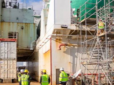 Construction workers in safety gear working on a large industrial site with scaffolding and machiner.