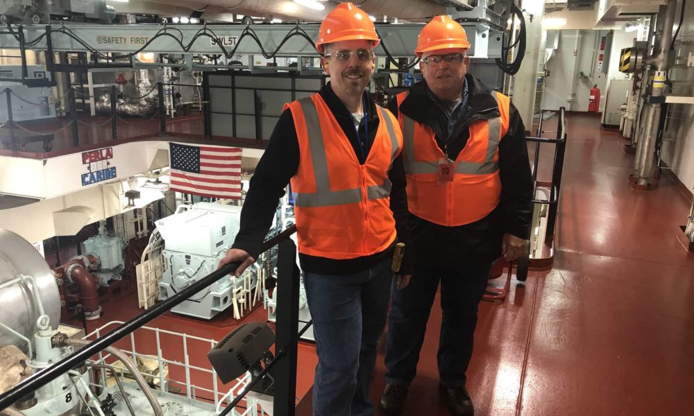 Hard hats and safety vests worn by two men in an industrial facility.
