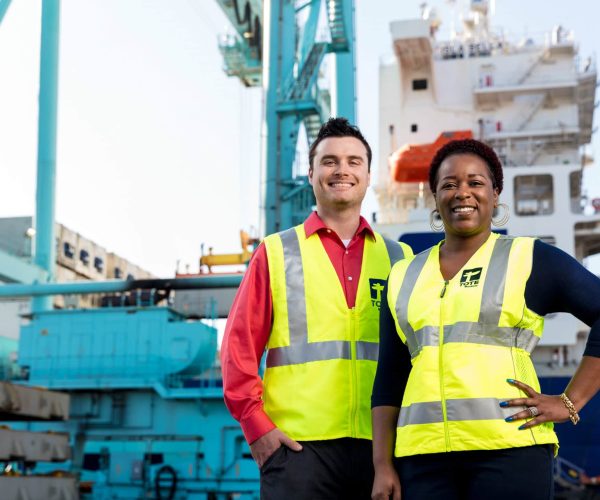 Crew members in safety vests standing on dock with ships in background.