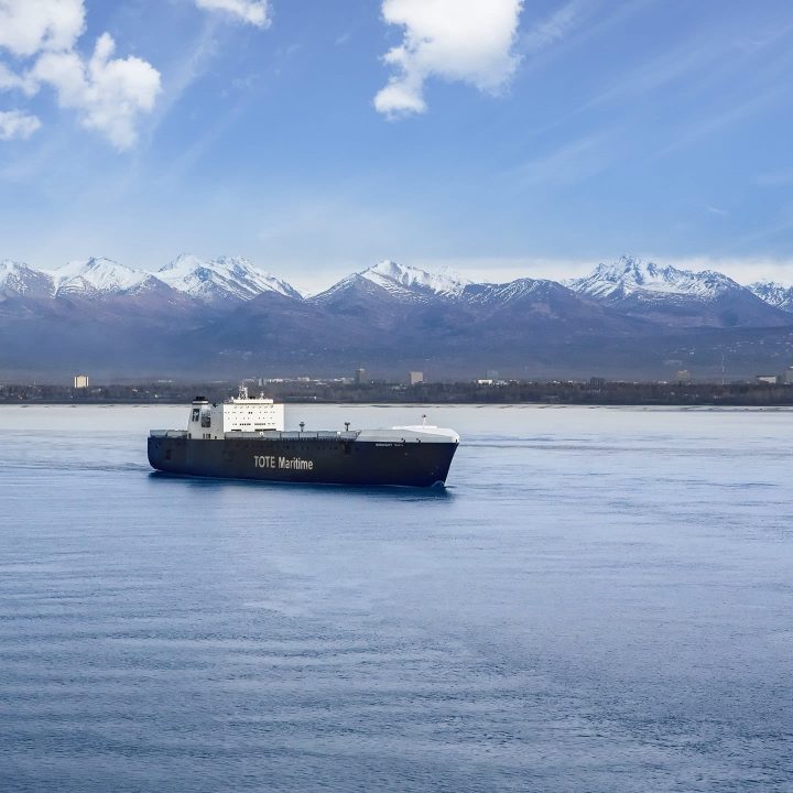 Tanker ship on calm water with snow-capped mountains in the background.