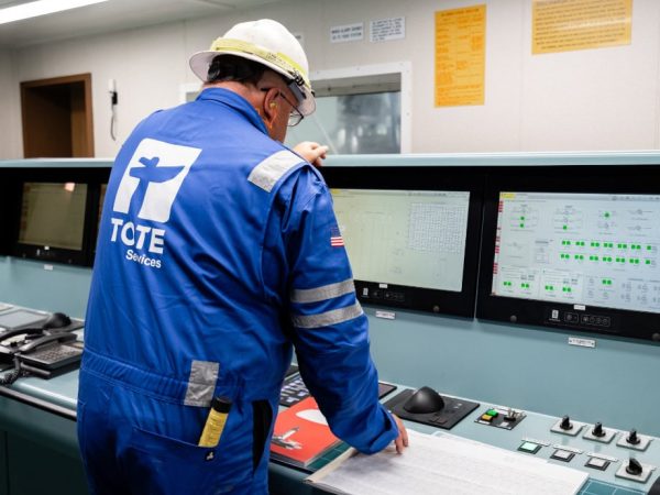 Worker in blue uniform operating control panels in an industrial setting.