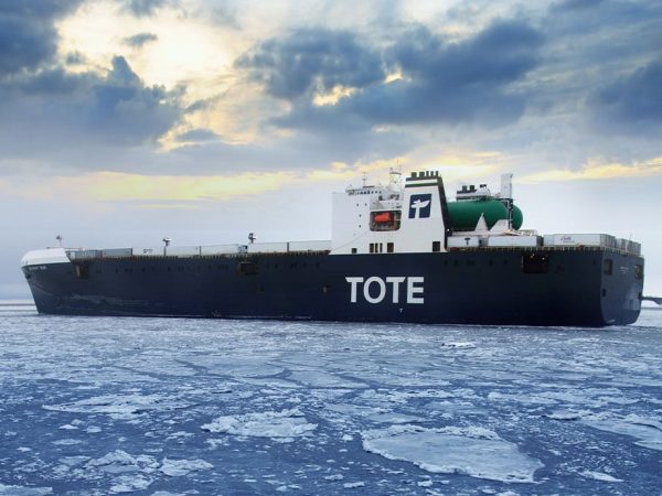 TOTE cargo ship sailing through icy waters under cloudy sky.
