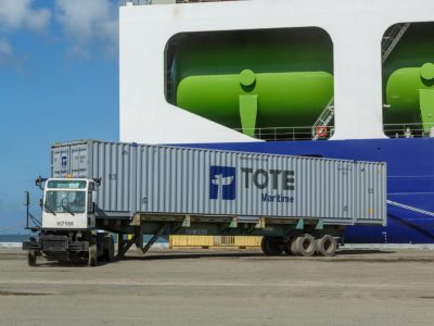 Cargo ship with green tanks and a truck on the dock.