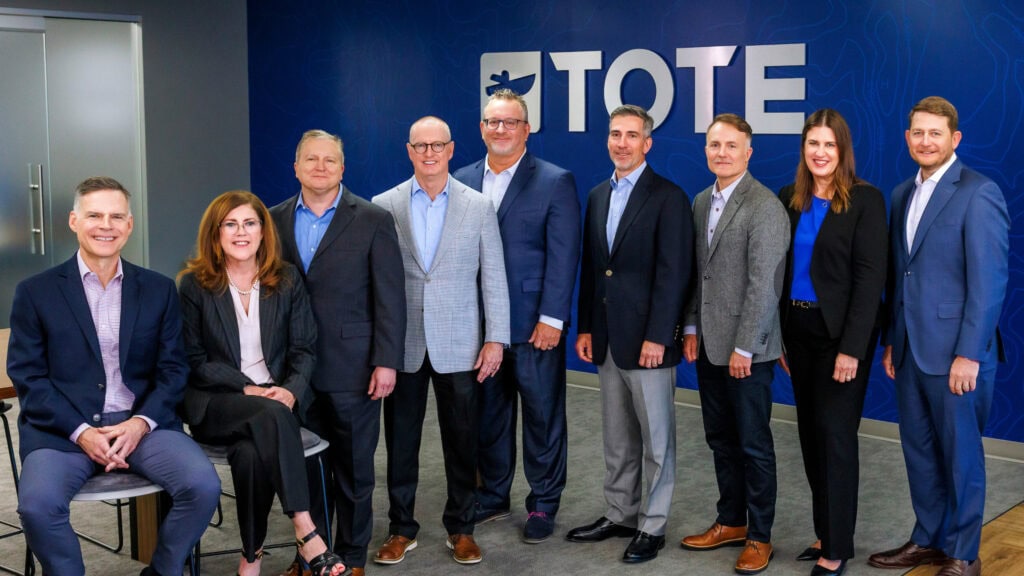 TOTE group of eight professionals standing in front of a blue wall with the TOTE logo.